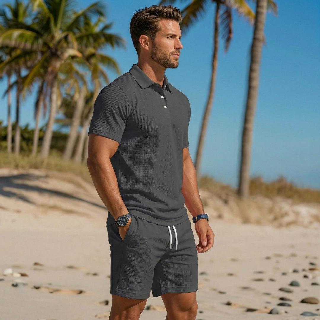 Ensemble homme polo col boutonné gris foncé porté de profil sur la plage