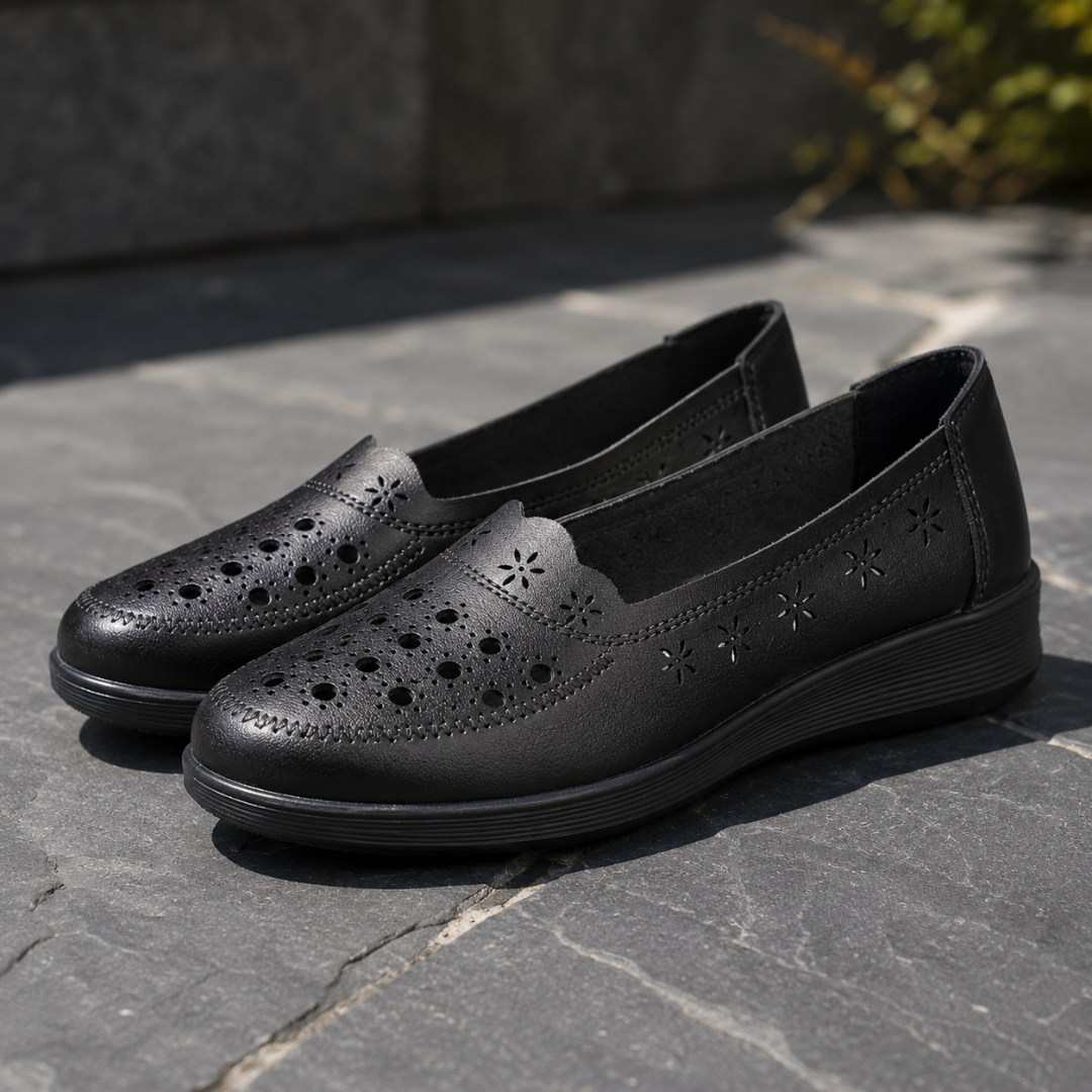 Mocassins noirs ajourés de fleurettes, semelle compensée nervurée, posés sur dalle sombre