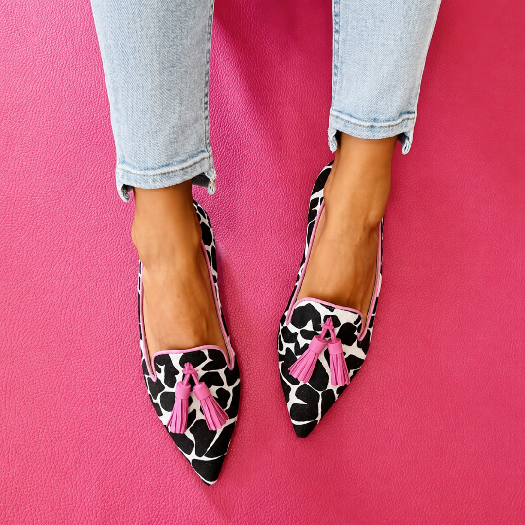 Mocassins imprimé vache avec pompons rose clair, portés sur fond rose vif