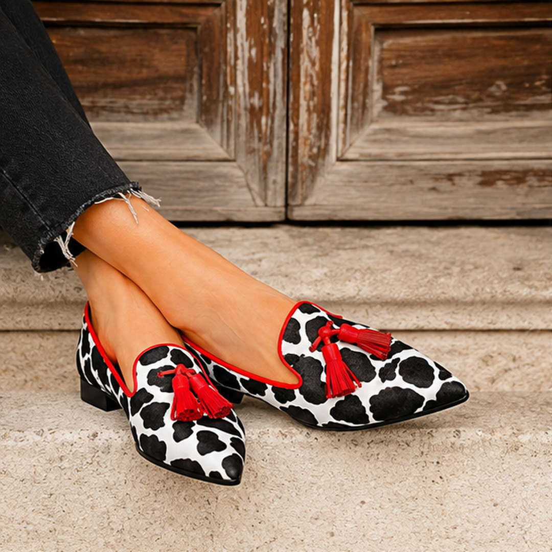 Mocassins femme à bout pointu, imprimé vache et pompons rouges, portés jambes croisées