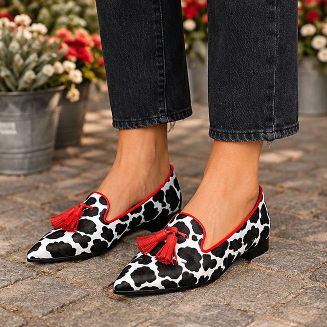 Mocassins imprimé vache avec liseré rouge et pompons, portés avec un pantalon gris