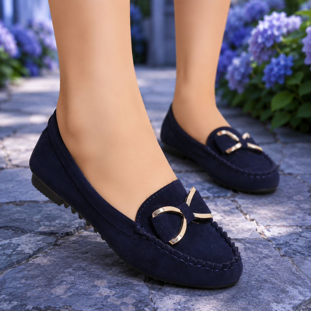 Mocassins bleu marine plats avec nœud doré, portés devant des hortensias en fleurs