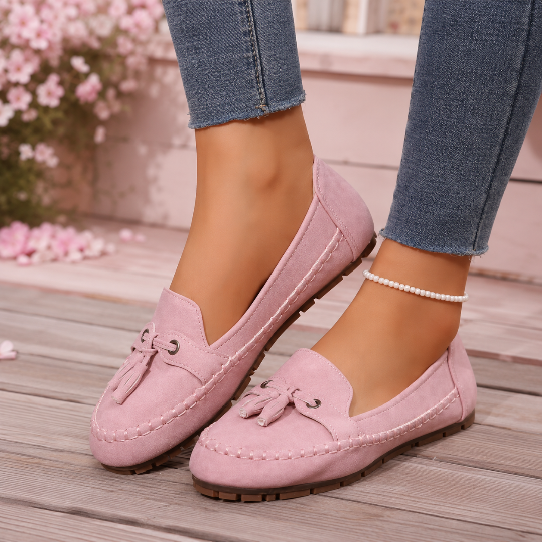Mocassins femme plats rose poudré portés avec un pantalon bleu, pompons noués et surpiqûres claires