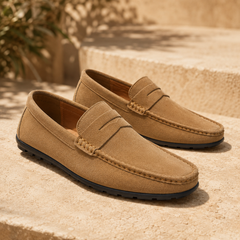Mocassins homme marron clair à bande penny, surpiqûres et semelle sombre, ambiance ensoleillée.