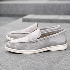 Mocassins homme gris, col souple ouvert et semelle blanche contrastante sur escalier