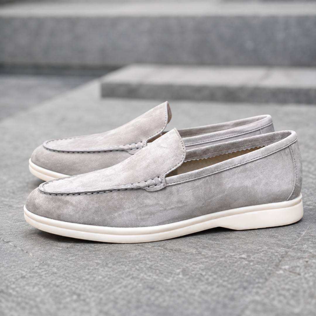 Mocassins homme gris, col souple ouvert et semelle blanche contrastante sur escalier