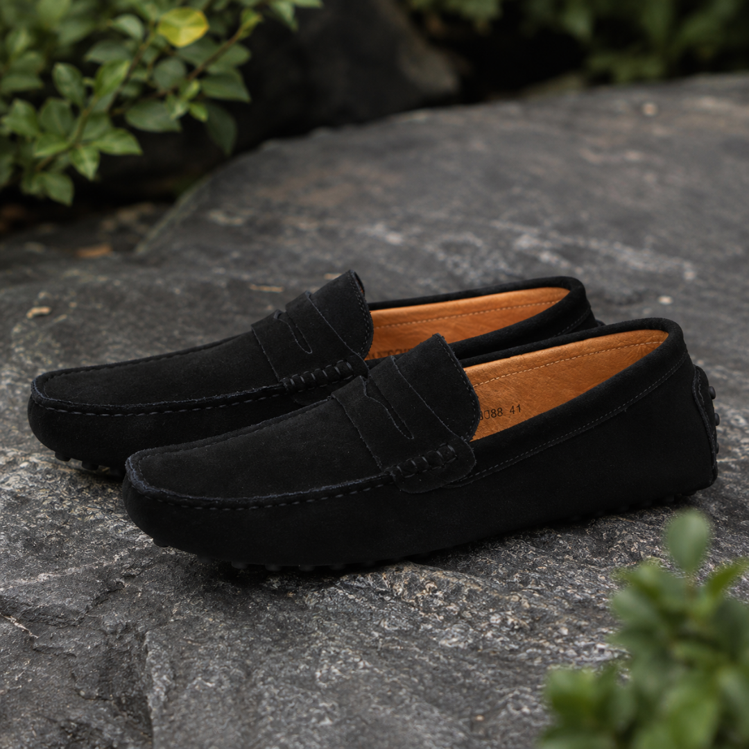 Mocassins homme noirs posés sur une pierre sombre, intérieur clair et bout arrondi