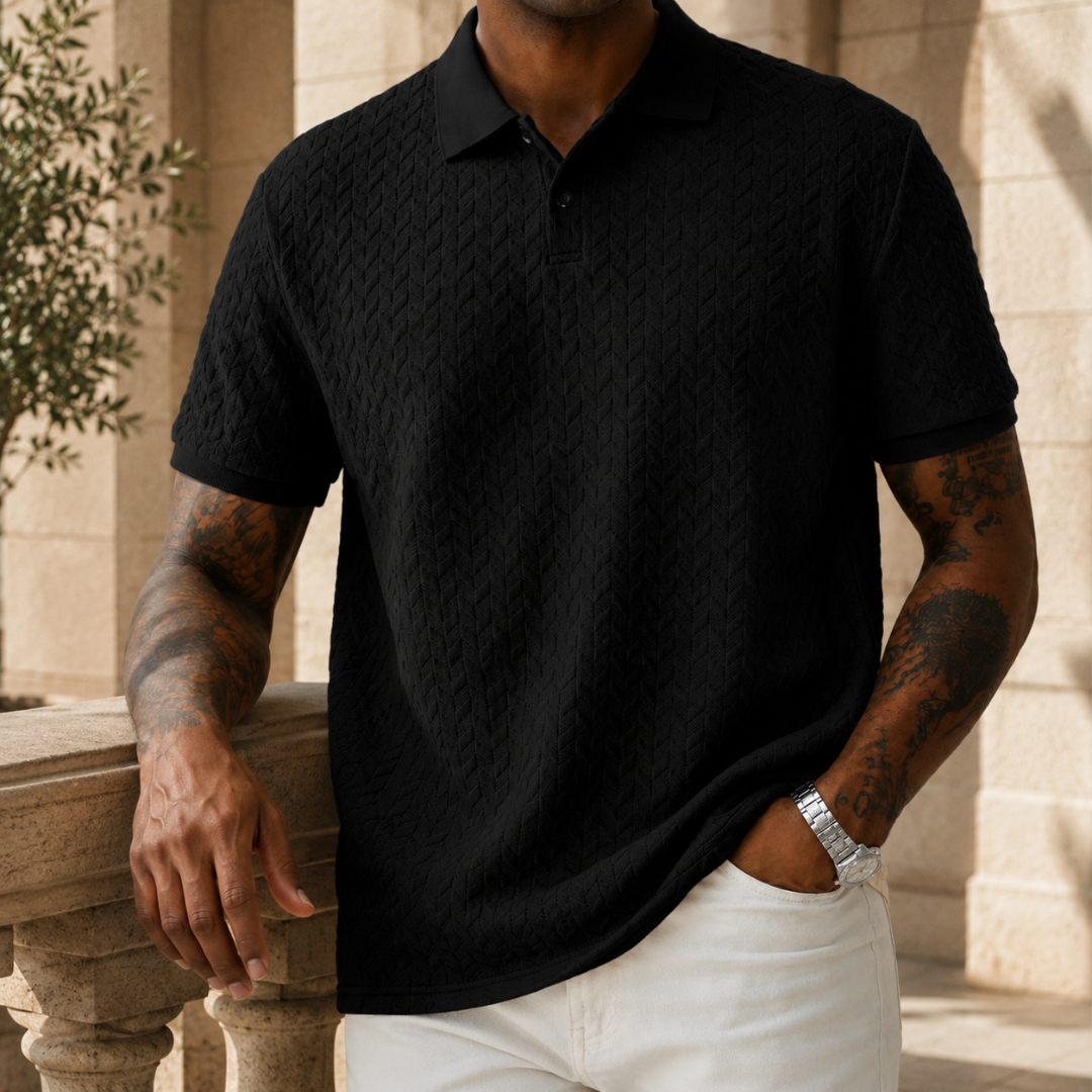 Polo noir à maille texturée, homme debout mains jointes devant lui, style épuré