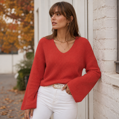 Pull rouge à col V en maille côtelée, manches longues évasées sur pantalon blanc