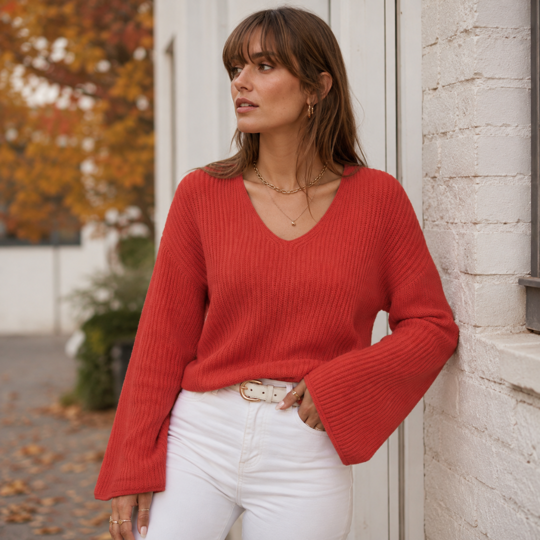 Pull rouge à col V en maille côtelée, manches longues évasées sur pantalon blanc