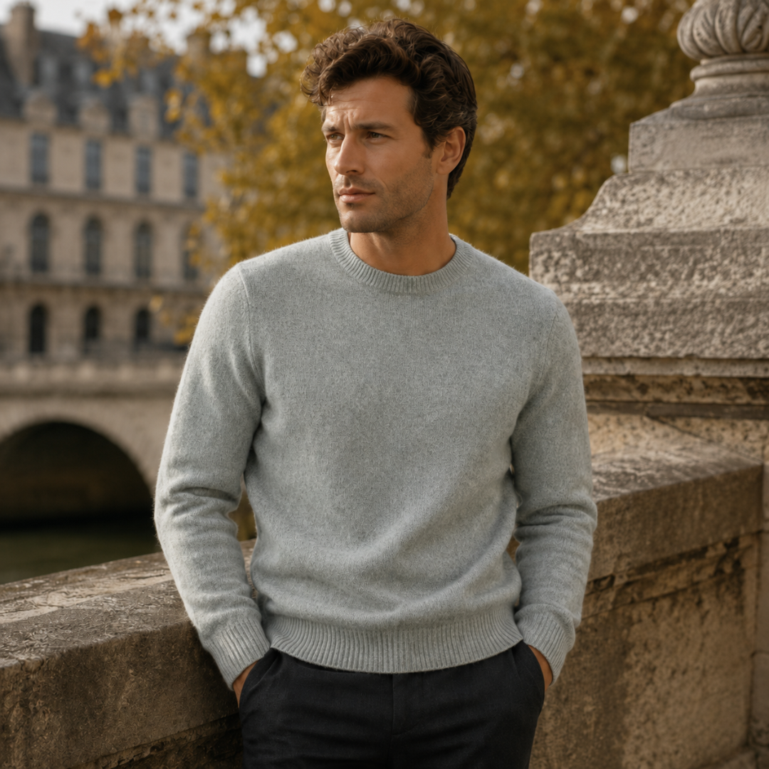 Pull homme vert gris à col rond côtelé, appuyé contre un parapet