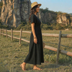 Femme en robe longue noire fluide marchant dans un paysage champêtre