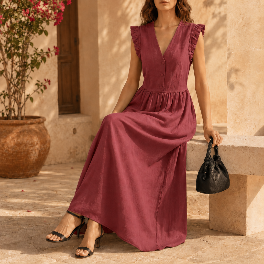 Femme élégante en robe longue rouge, sac noir à la main, devant un mur en pierre
