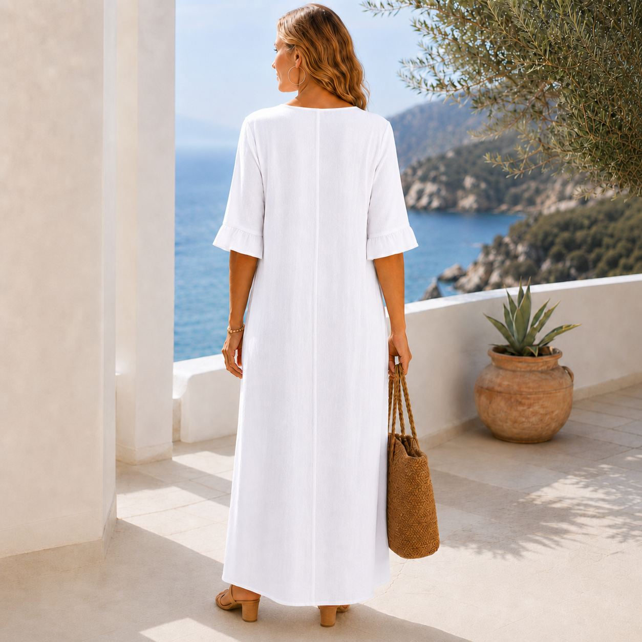 Femme en robe maxi blanche col V tenant un sac blanc dans un patio méditerranéen