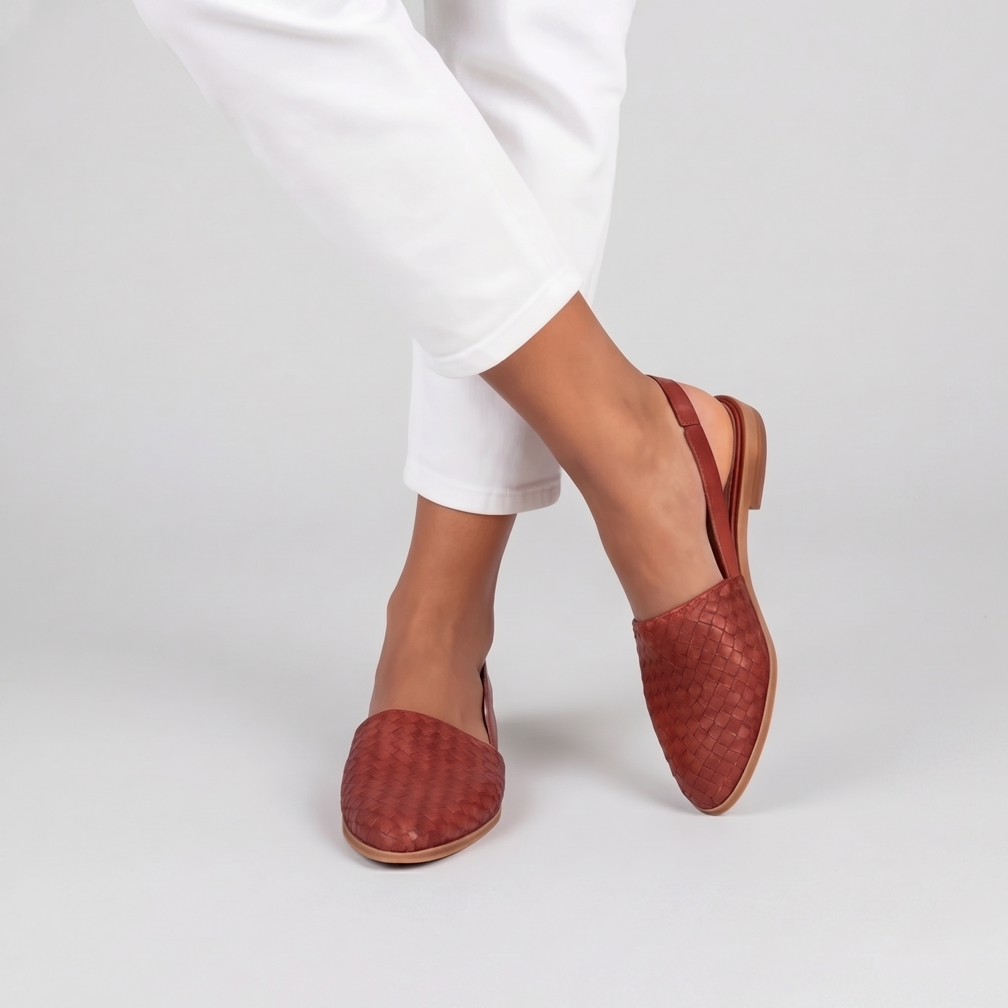 Sandales plates tressées femme rouge terracotta portées jambes croisées semelle claire