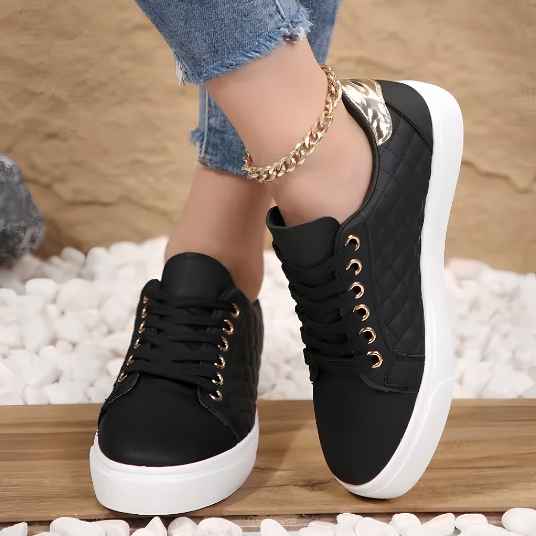 Paire de sneakers noires Clarice posée sur fond extérieur, semelle plateforme et œillets dorés visibles