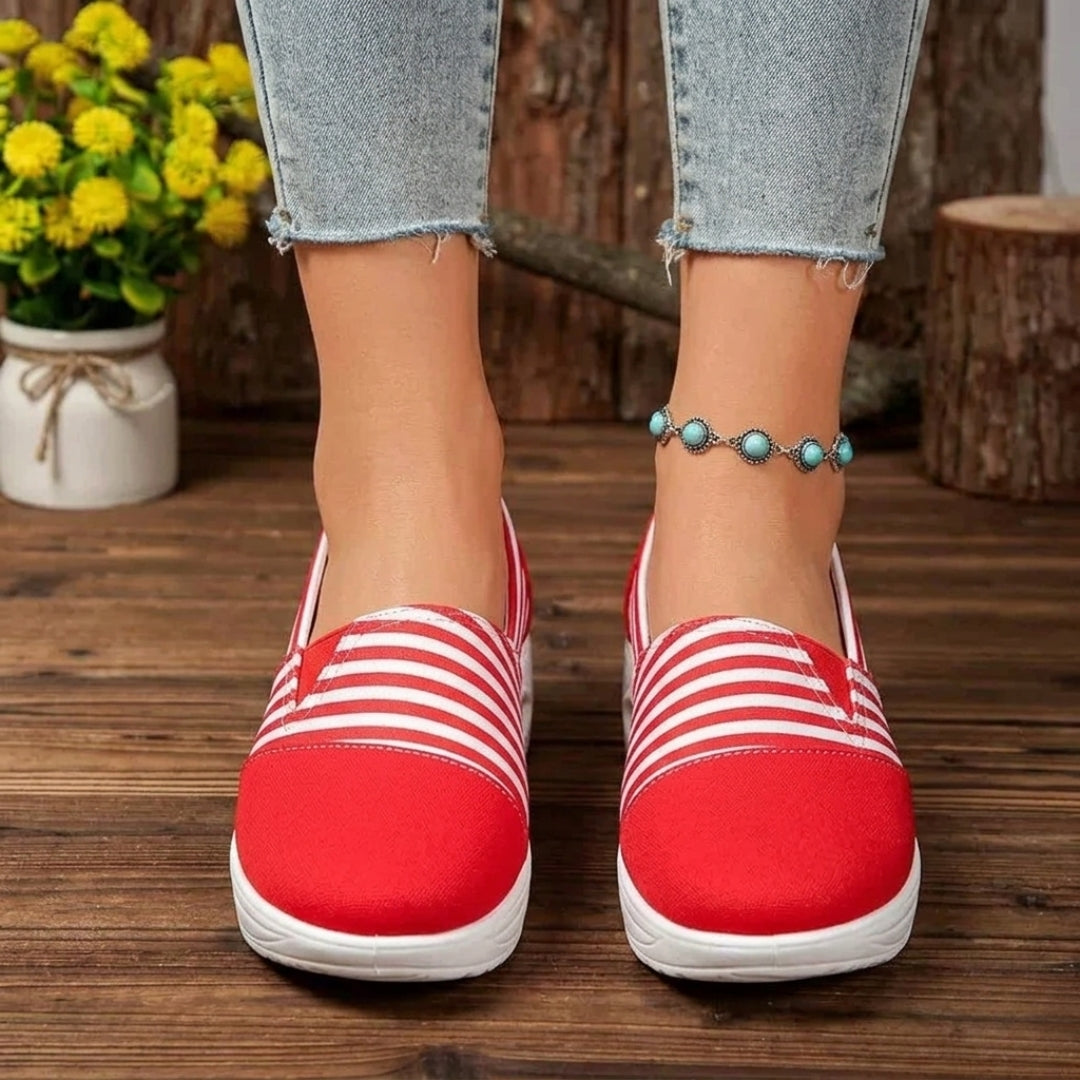Sneakers femme slip-on rayées rouge portées de profil sur parquet en bois