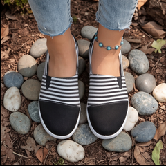 Sneakers slip-on noires rayées blanches vues de dessus, entourées de galets gris