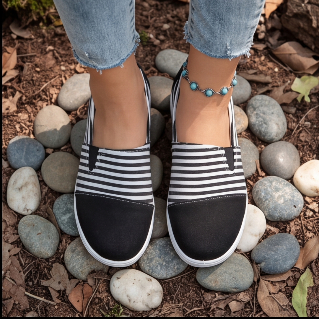 Sneakers slip-on noires rayées blanches vues de dessus, entourées de galets gris