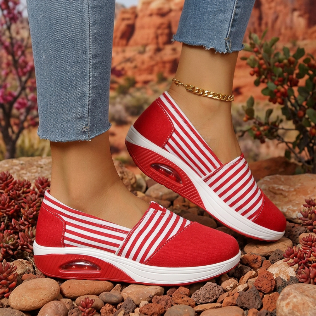 Sneakers slip-on femme rouges à rayures blanches portées avec un jean sur rochers