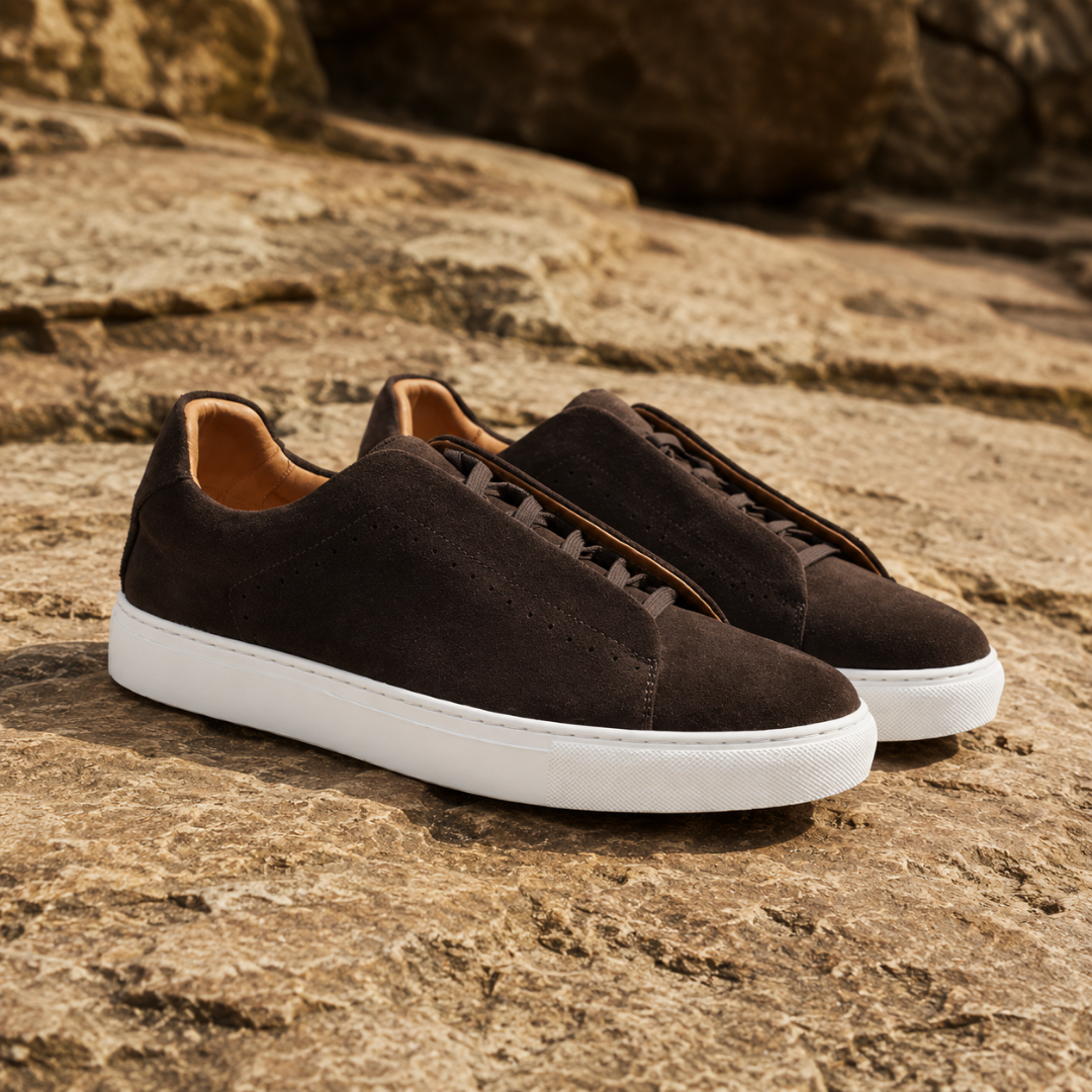 Paire de sneakers homme marron foncé posée sur la roche, semelle blanche
