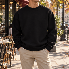Sweat homme noir à col rond porté avec un pantalon beige en terrasse