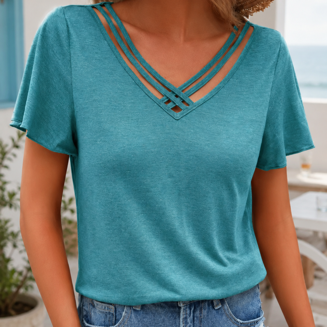 T-shirt femme bleu clair, col V à lanières croisées, posé devant la plage en été
